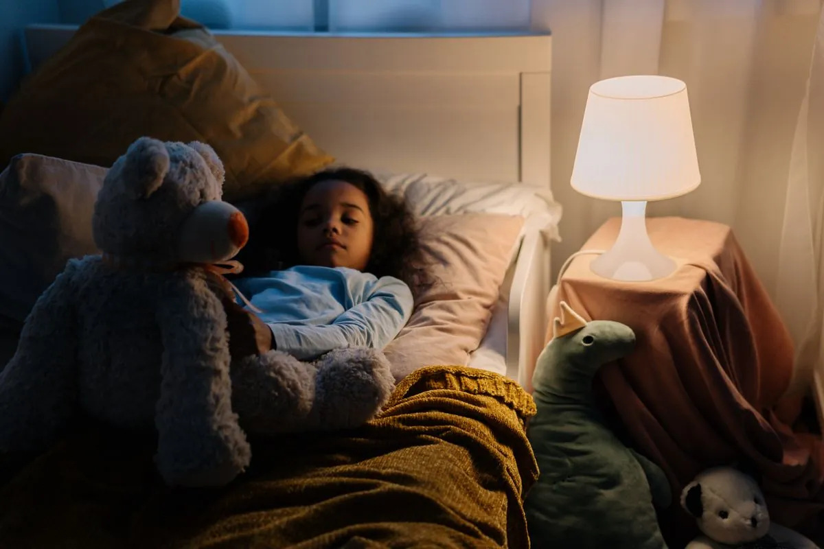 Ett barn som ligger vaket i sängen med gosedjur och en tänd nattlampa