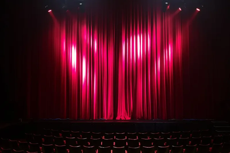 En tom teatersalong med röd ridå och stolsrader